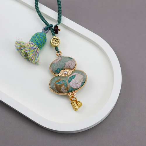 Soft green floral brocade gourd bag charm with a green cord, multicolored tassel and gold-tone decorative details.